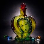 Cor Vitae heart-shaped glass bottle with inner face, red stopper, and golden-green tones