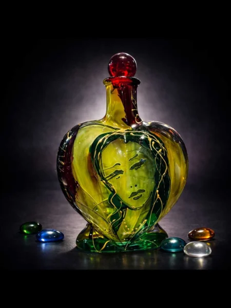 Cor Vitae heart-shaped glass bottle with inner face, red stopper, and golden-green tones